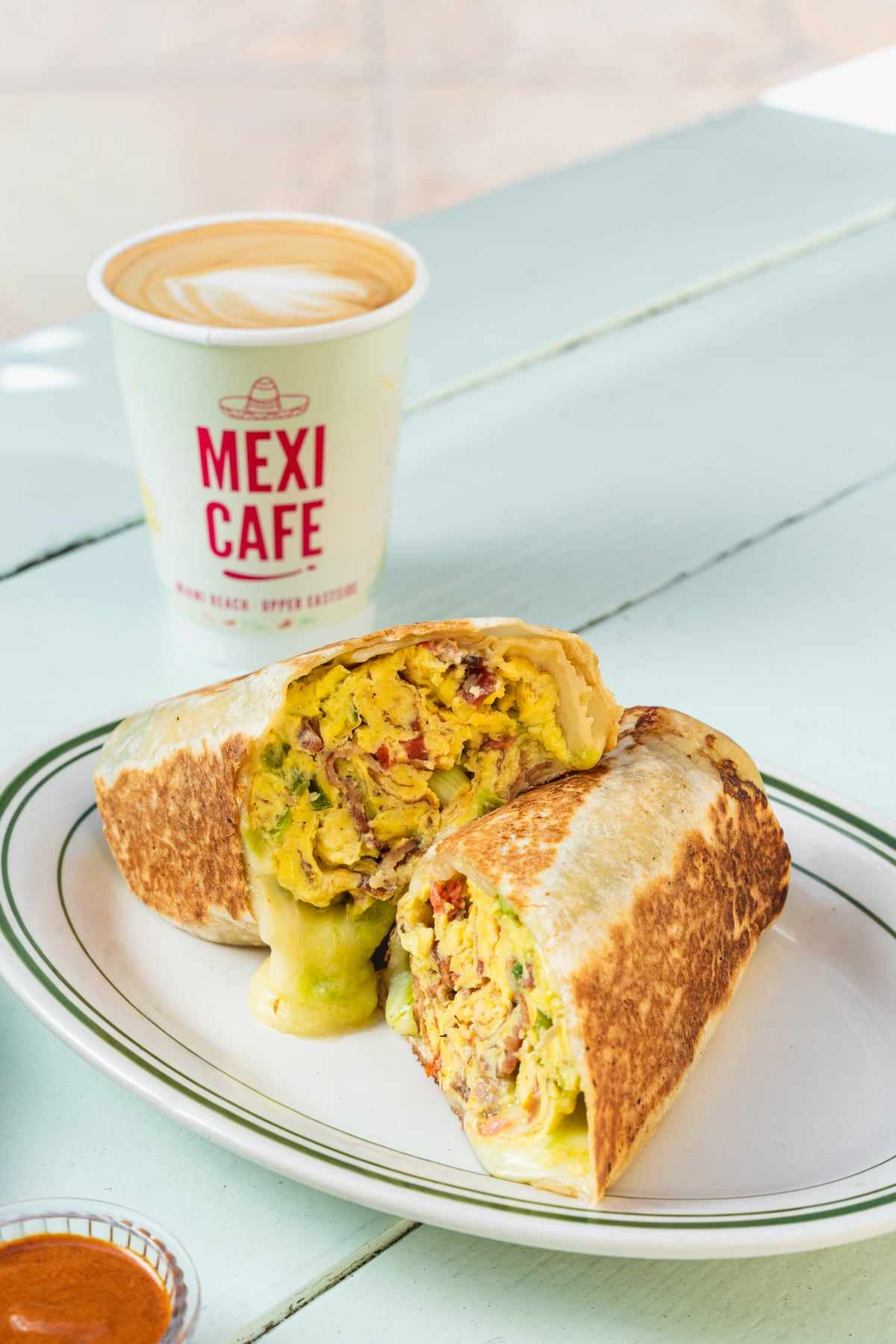 The morning burrito cut in half showing egg, bacon and avocado, next to a Mexi Cafe coffee cup