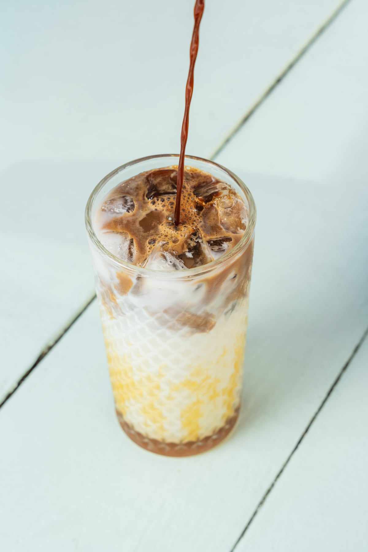 An iced latte in a tall glass, espresso poured over milk and ice