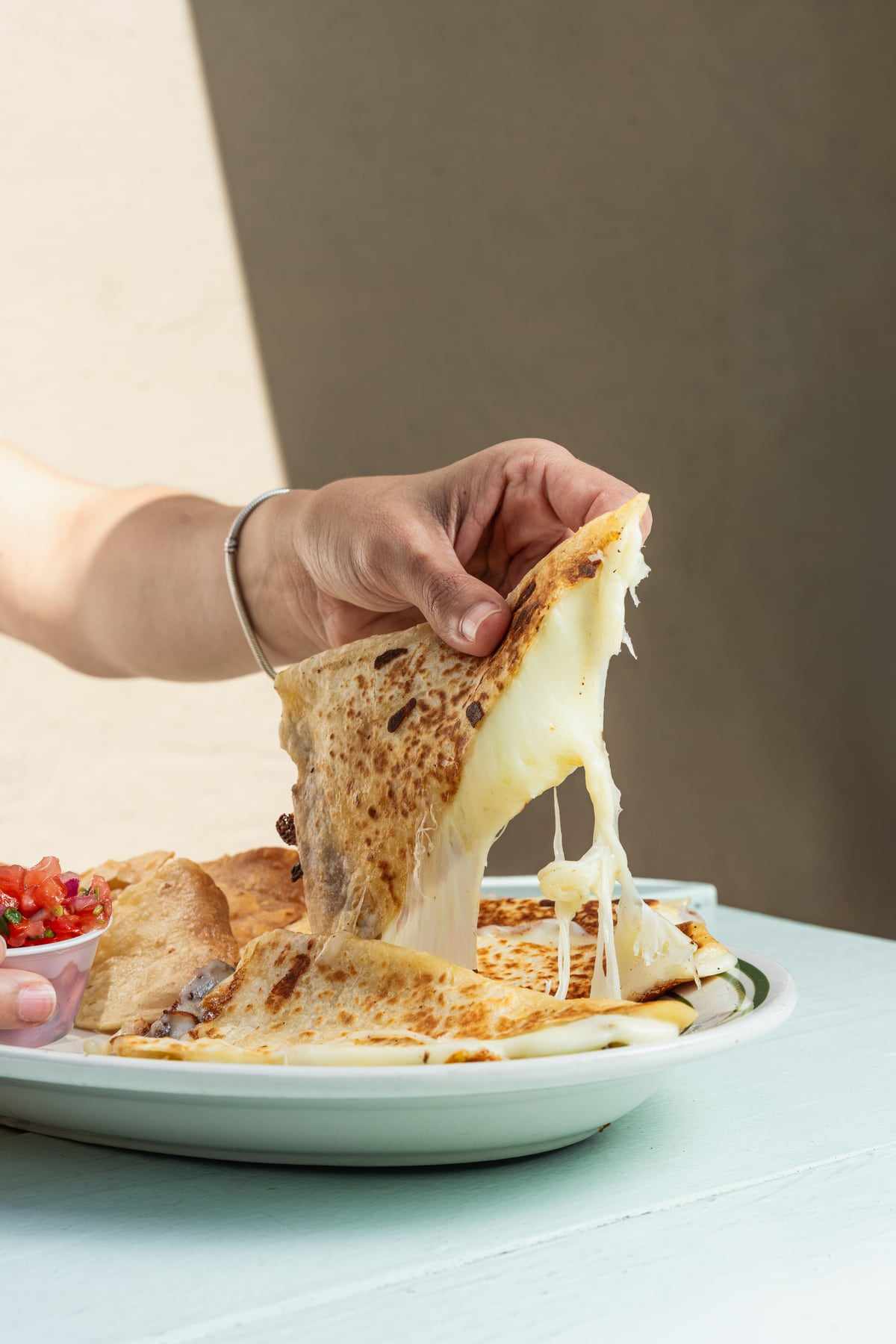 A quesadilla wedge lifted from the plate with the cheese stretching